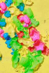 Scattered colorful play shapes mixed with kinetic sand on a yellow carpet.