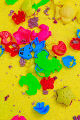 Scattered colorful play shapes mixed with kinetic sand on a yellow carpet.