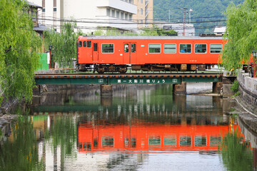 Bright red local train is reflected in the canal as it crossed the bridge at Kinosaki Onsen
