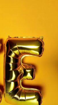 Three golden letter balloons forming the word 'LIE' floating against a solid yellow backdrop in a well-lit studio setting.