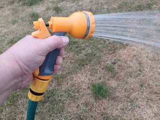 Man watering parched grass with a hose gun
