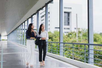 Fototapeta premium Two businesswomen walking and talking on a modern skybridge