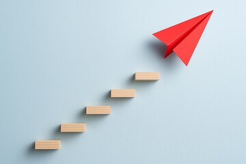 Red paper airplane ascends wooden block steps on blue