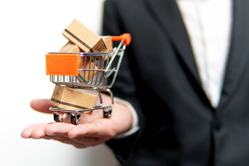 Businessman holding miniature shopping cart full of cardboard boxes