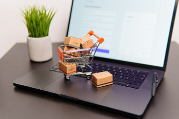 Shopping cart full of cardboard boxes standing on laptop keyboard is representing online shopping