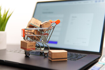 Shopping cart full of cardboard boxes standing on a laptop keyboard is representing online shopping