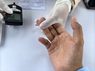 Close-up of a medical worker performing a blood sugar test using a glucometer on a man's fingertip during a health check.