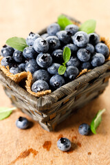 Ripe blueberries in wicker basket on wooden table.