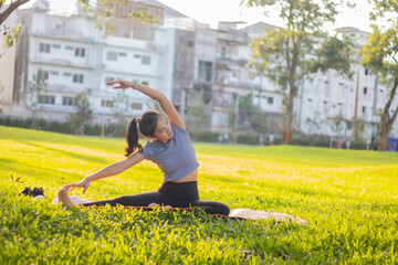 A young woman practices yoga outdoors in a city park, staying in a lotus pose, calm, relaxed,...