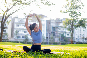 A young woman practices yoga outdoors in a city park, staying in a lotus pose, calm, relaxed,...