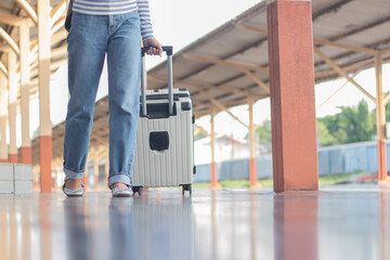 A cool young woman walks alone through a city train station, dragging her suitcase with...