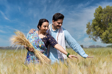 Smiling couple with bunch of wheat and standing amidst crops in agricultural field.