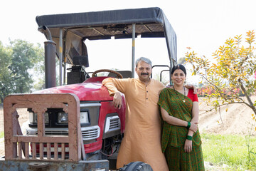 Happy Indian couple with tractor on agriculture field