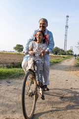Portrait of Indian farmer with daughter riding bicycle on rural road
