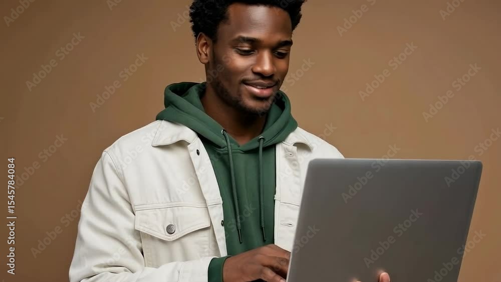 Poster a smiling man uses a laptop computer while standing against a brown background