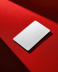 A blank white card rests on a vibrant red surface, diagonally intersected by a beam of light casting a subtle shadow
