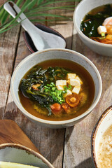 Miso soup with tofu and mushrooms, bright natural lighting, overhead rustic wood composition