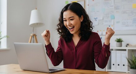 Happy businesswoman celebrates success on laptop computer at office desk feeling joy and achievement
