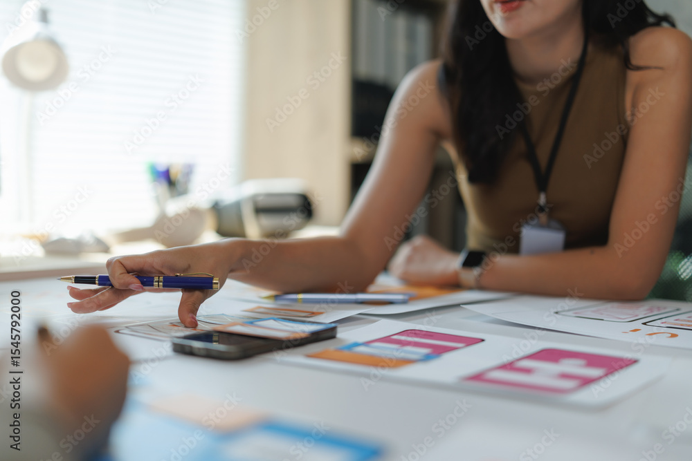 Poster web designer pointing at a mobile phone layout during a meeting