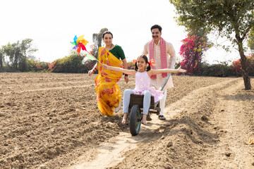 Parents and daughter having fun on push cart over agricultural field.