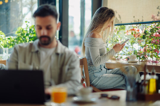 Freelancer woman using smartphone in cafe while man works on laptop