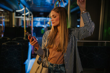Young woman using smartphone while standing on bus at night