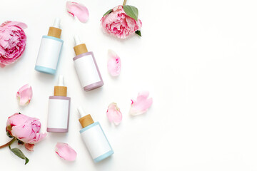 Essential oil bottles and pink flowers arranged on white background