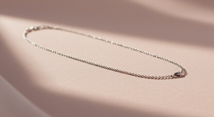 Delicate silver chain necklace on a soft pink surface with subtle shadow play