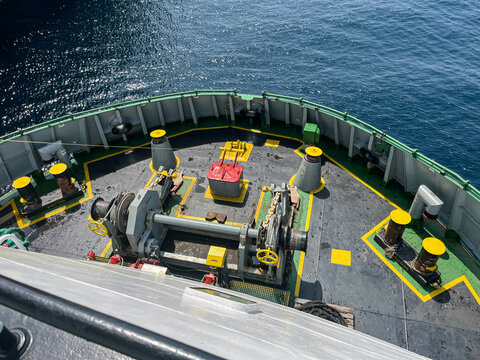 Detailed View of Ship&rsquo;s Forward Mooring Station with Mooring Winch, Split Drum, Anchor Chain, Bollards, Fairleads, Cleats, and Chocks on Steel Deck at Sea during Daytime Vessel Operation