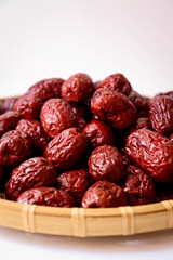 Dried red jujubes in a bamboo tray. White background.