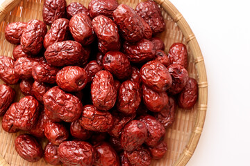 Dried red jujubes in a bamboo tray. White background.