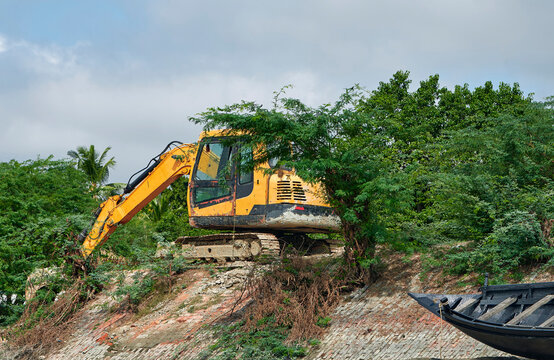 a backhoe excavator digging soil near river embankment at a village in Gosaba, Sundarbans delta in West Bengal.