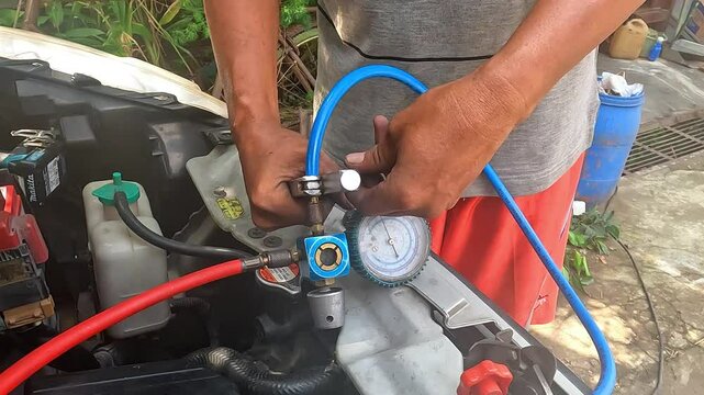 Auto mechanic checking car AC refrigerant pressure with gauge to detect leakage. Vehicle air conditioning maintenance and freon level inspection in a garage.