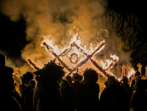 People in traditional Latvian costumes and wreaths watching burning structure shaped as latvian traditional austras tree ornament at Midsummer celebration