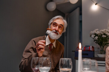 An elderly man smiles while savoring a meal, surrounded by elegant decor and warm lighting,...
