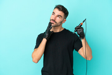 Young tattoo artist man isolated on blue background looking up while smiling