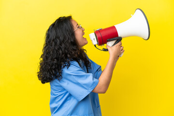 Young surgeon doctor asian woman isolated on yellow background shouting through a megaphone