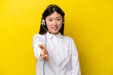 Telemarketer Chinese woman working with a headset isolated on yellow background shaking hands for...