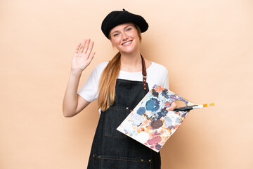 Young artist caucasian woman holding a palette isolated on beige background saluting with hand with...