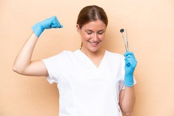 Dentist caucasian woman holding tools isolated on beige background doing strong gesture