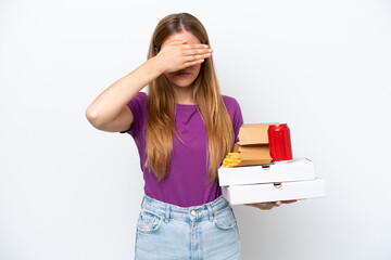 Young pretty blonde woman holding fast food isolated on white background covering eyes by hands. Do...