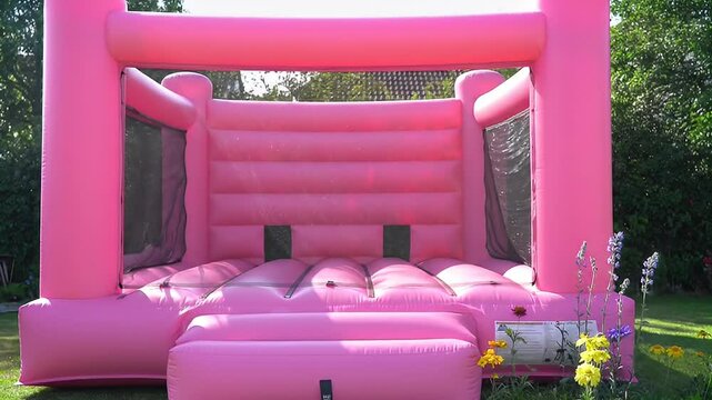 Pink inflatable bounce house in a yard with flowers