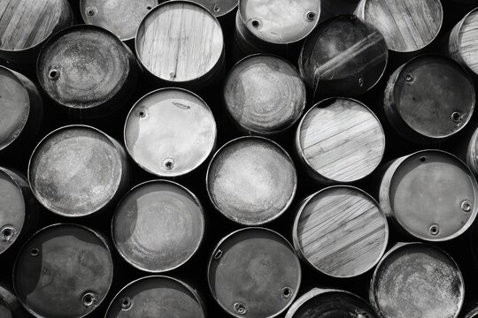 A monochrome close-up showcases a dense arrangement of weathered, cylindrical metal drums, exhibiting varying degrees of wear and discoloration