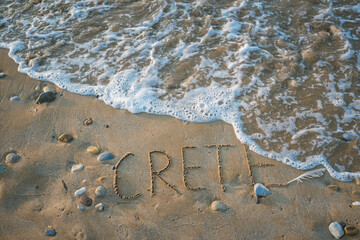 Word Crete being washed away by sea foam on sandy beach. The concept of tourism on this beautiful paradise island