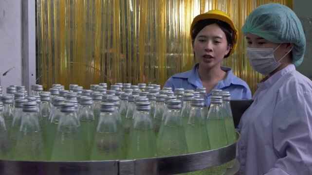Quality control woman and manager wearing a lab coat to checking juice industrial process at factory. Teamwork at production line successful concept.	