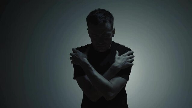 Man hugging himself in darkness, concept of self-love and emotional pain