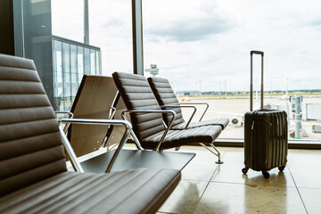 Empty airport seats next to a window with a piece of luggage, capturing a traveler's moment of...
