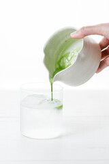 fresh matcha tea, green tea pouring on a glass of coconut water on white wooden table.