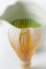 Cup of fresh matcha tea, green tea and Chasen, bamboo whisk, on white wooden table.