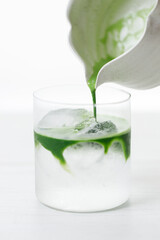 fresh matcha tea, green tea pouring on a glass of coconut water on white wooden table.